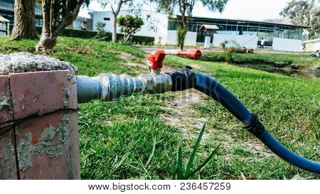 Hose Connected To The Water Pipe On The Green Grass. The Hose Is Blue And The Silver Pipe With Red K