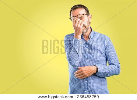 Handsome middle age man with sleepy expression, being overworked and tired, rubbes nose because of weariness