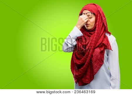 Young arab woman wearing hijab with sleepy expression, being overworked and tired, rubbes nose because of weariness