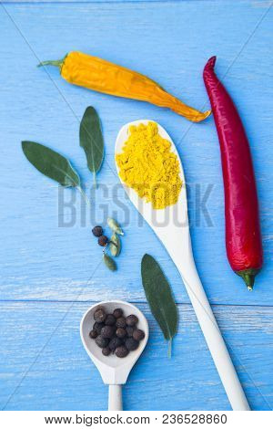 Cooking Hot Spicy Food Concept. Dry Spices And Herbs In Wooden Spoons And Chili Peppers On Blue Wood