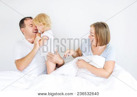 Happy And Loving Family Morning Concept. Cheerful Parents In Sleepwear Having Fun With Their Daughte