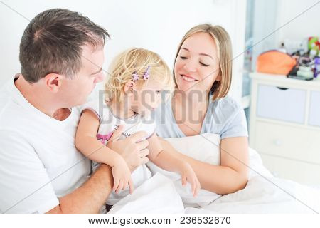 Happy And Loving Family Morning Concept. Cheerful Parents In Sleepwear Having Fun With Their Daughte