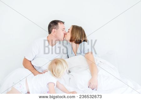 Happy And Loving Family Morning Concept. Kissing Parents In Sleepwear And Back View Daughter On The 