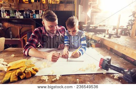 family, carpentry, woodwork and people concept - happy father and little son with blueprint at workshop