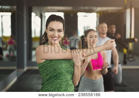 Young Smiling Woman Stretching Hands In Fitness Club. Cheerful Female Fitness Coach Warming Up, Prep
