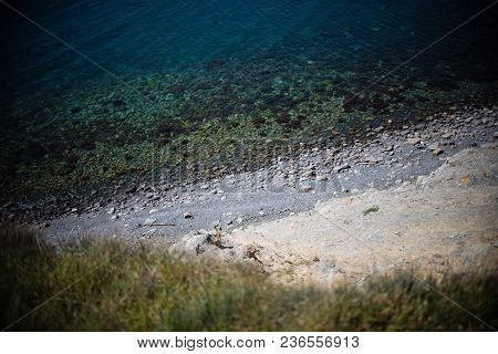 The Sea And The Beach With Stones Are At The Bottom. Man Watching From The Cliff