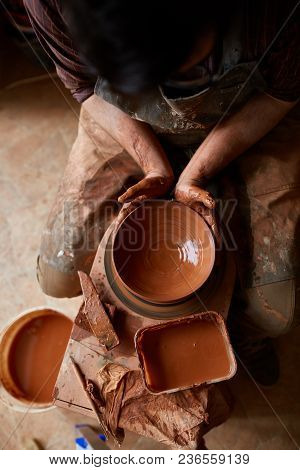 A Male Potter In Plaid Shirt And Dirty Apron Who Molds Bowl From Clay, Selective Focus, Close-up. Cr
