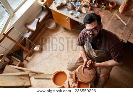 Portrait Of A Handsome Bearded Male Potter In Plaid Shirt And Dirty Apron Who Molds Bowl From Clay, 