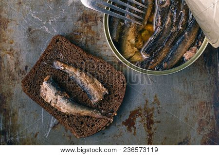 Canned Sprats In Tin Can With Rye Bread. On Rustic Background