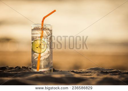 Picture Of A Glass Of Gin Tonic With Straw And Lime Slice On The Beach, At Sunset. Long Beach, Ko La