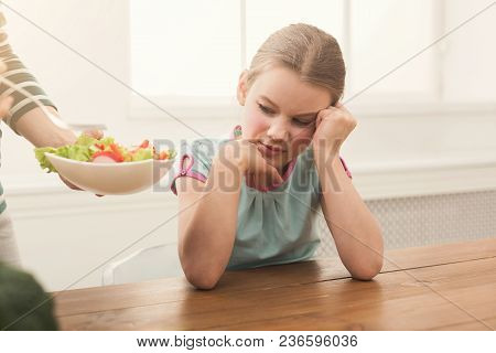 Woman Offering Her Daughter Salad But Girl Refusing Eating In The Kitchen Over Window. Healthy Food 