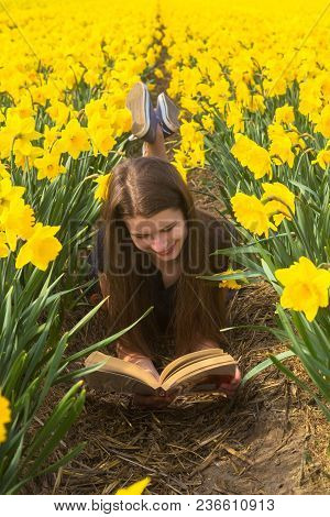 Happy Young Teenager Girl Reads Book Among Flowers. Adorable Teenager Girl Having Fun In Flowering D