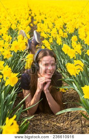 Teen Girl Listening To Music On Headphones. A Young Girl On A Day Off Rests Outside The City, On Flo