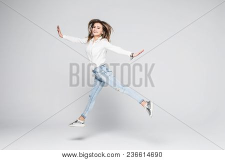 Smiling Young Woman Jumping In Air With Raised Fists Over White Background