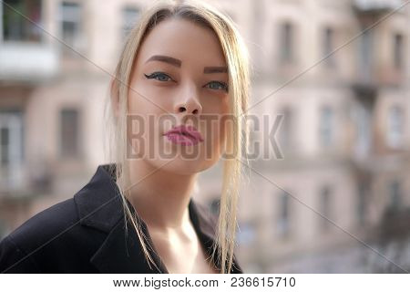 Portrait Of A Young Woman In A Black Suit Close-up Against A Background Of A Blurry City In The Rays