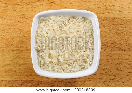 Overhead Shot Of Raw Basmati Rice In A White Bowl On A Wooden Board Background. Basmati Rice Is A Va