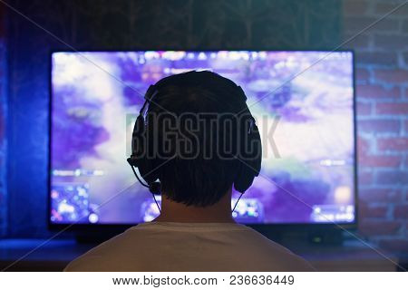 Gamer Or Streamer In Earphones With Microphone Sits At Home In Dark Room And Plays With Friends On N
