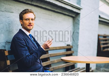 Businessman In Solid Suti Sitting On Bench And Smoking Cigarette After Tasty Lunch.