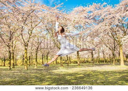 Happy Teenager He Is Laughing And Jumping Up. Teen Girl In Spring Blossoming Garden. Teenager And Bl