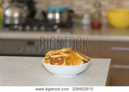 White Plate Full Of Pancakes Standing On A Table Against Kitchen Utensils