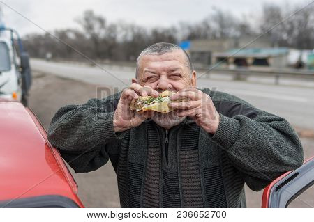 Portrait Of Caucasian Senior Driver Eating Lyulya Kebab In Lavash Near His Car