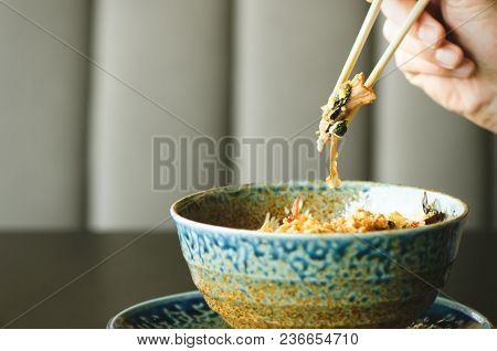 Man's Hand Holding Chopsticks Over A Plate Of Japanese, Thai, Chinese Meal - Rice, Mushroom, Vegetab