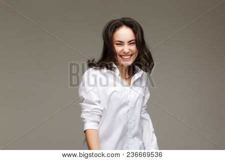 Beautiful Girl In A White Shirt Shows Emotions - Smile, Fun. On A Light Background.