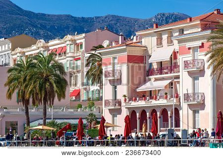 MENTON, FRANCE - MARCH 11, 2017: People dinning in outdoor restaurant as colorful buildings on background on promenade of Menton - small town on French Riviera,  popular travel destination.
