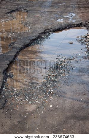 The Bad Asphalted Road. Big Pothole Filled With Water. Dangerous Destroyed Roadbed. Mirror Reflectio