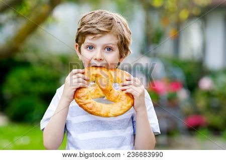 Adorable Little Kid Boy Eating Huge Big Bavarian German Pretzel. Happy Blond Child Enjoying Tasteful