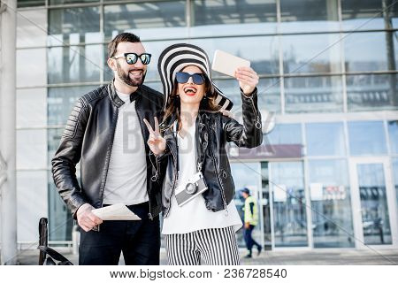 Young Couple Of Travelers In Leather Jackets Making Selfie Photo Standing In Front Of The Airport Te