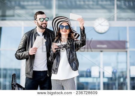 Young Couple Of Travelers In Leather Jackets Making Selfie Photo Standing In Front Of The Airport Te