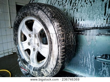 Car Wash. Foam Drains Down And Dissolves Dirt On The Rear Door And Spare Wheel Of The Car.
