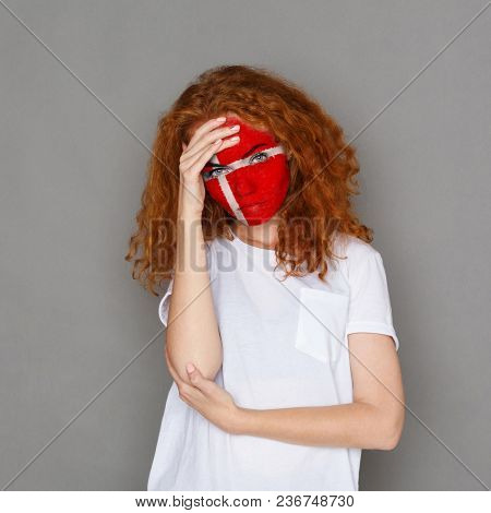 Face Of Young Sad Woman Painted With Flag Of Denmark. Football Or Soccer Team Fan, Sport Event, Face