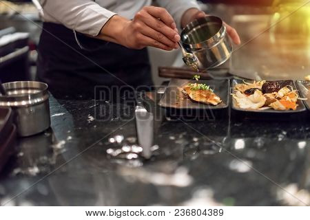Hand Of Chef Adding Spring Onion On Fish Steak In Front Of Customers. Japanese Tepanyaki Steak