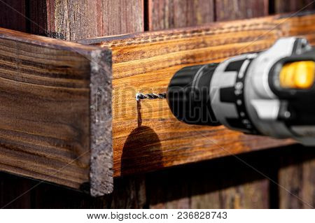 Glazed Board Is Pre-drilled. Battery Drill Drills A Hole In A Brown Glazed Wooden Board