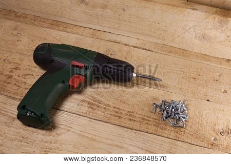 Cordless Screwdriver With Screws On Wooden Floor. Close-up