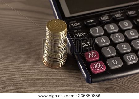 Stack Of Coins And Calculator On A Wooden Surface