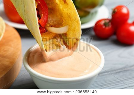 Fish taco dipped in sauceboat with tasty creamy tomato sauce on wooden table