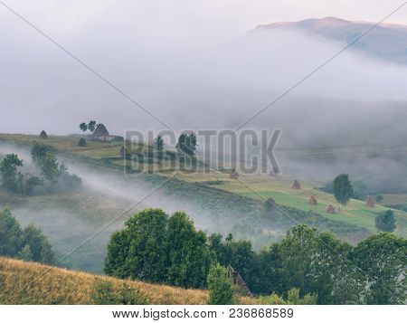 Beautiful Mountain Landscape With And Old House, Trees,and Haystacks In A Foggy Morning, Dumesti, Sa