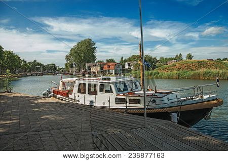 Boat In A Pier At The Foreground, Vecht River With Bridge And Brick Houses On A Sunny Day In Weesp. 