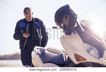 A Middle-aged Man Takes A Break On The Road Near The Lake Reading And Sends Text Messages On His Mob
