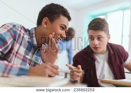 Smiling Multicultural High School Teenage Students Talking During Lesson And Teacher Standing Behind