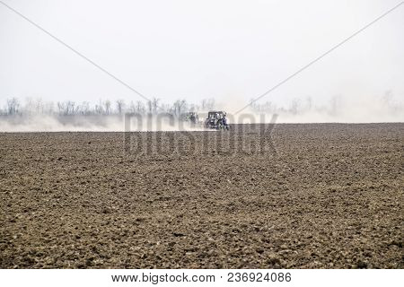 The Tractor Harrows The Soil On The Field And Creates A Cloud Of Dust Behind It.