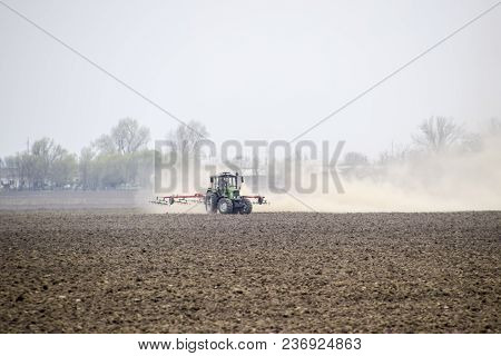 The Tractor Harrows The Soil On The Field And Creates A Cloud Of Dust Behind It.