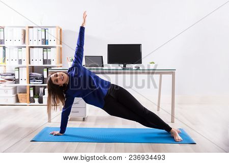 Young Businesswoman Doing Stretching Exercise On Exercise Mat At Workplace