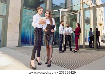 Business Lady. Office Staff. Two Young Girls With Electronic Tablets Communicate Against The Backgro