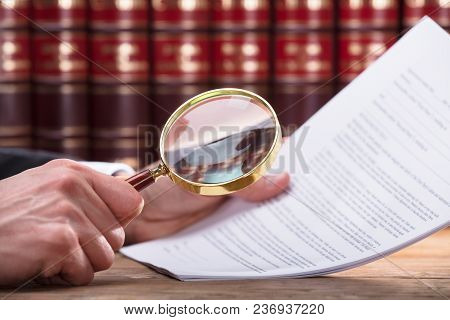 Human Hand Examining Document Through Magnifying Glass