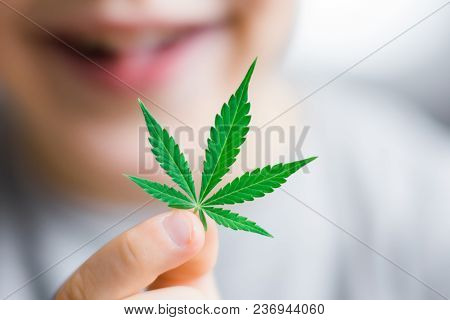 Smiling Kid Child Holding A Hemp Leaf. Concepts Of Using Marihuna For Medicinal Purposes For Childre