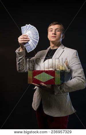 Young Prestidigitator Showing Tricks With Playing Cards And Magic Box In The Dark Room Cropped Shot